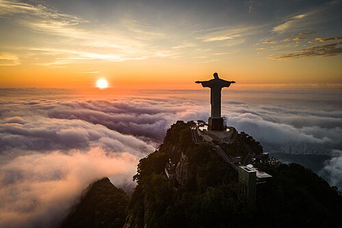 The image captures the iconic Christ the Redeemer (Cristo Redentor) statue towering over Rio de Janeiro in a breathtaking panoramic shot from above. Recognized as one of the New Seven Wonders of the World, the statue stands as one of Brazil’s most famous landmarks. Taken from a striking aerial perspective, the photo highlights the city's unique landscape, set between mountains and the bay, with exceptional lighting that enhances the interplay of light and shadow. This photograph was awarded first place in the "Wiki Loves Monuments 2025" contest.